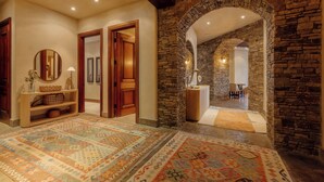 A hallway with a patterned rug, wooden doors, a stone wall, and a mirror. - See Forever Condo by InvitedHome | Ski Valet, Walk to Ski, Hot Tub, Balcony (Mountain Village)