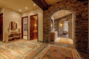 A hallway with a patterned rug, wooden doors, a stone wall, and a mirror. - See Forever Condo by InvitedHome | Walk to Hike and Festivals, Hot Tub, Balcony (Mountain Village)