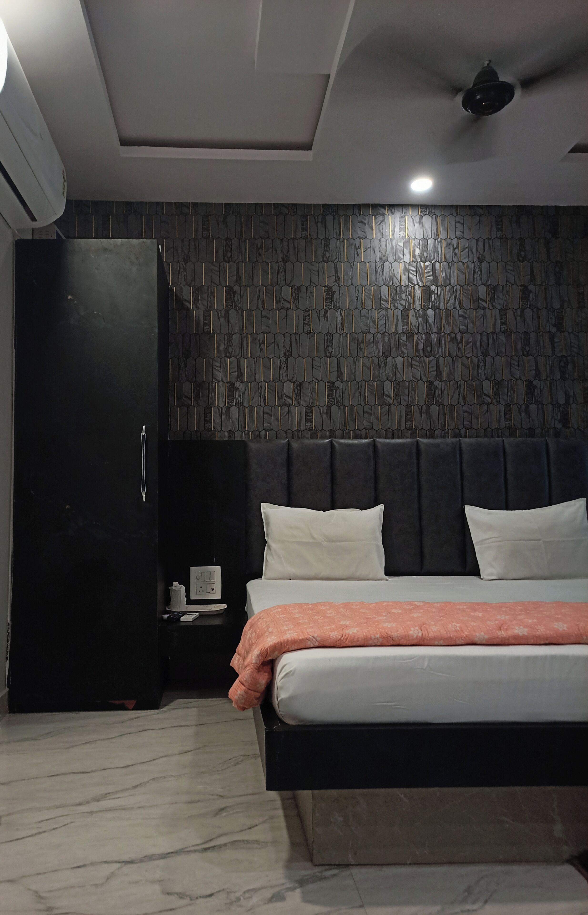 Un dormitorio moderno con cabecera oscura, cama con ropa de cama blanca y naranja, armario negro y suelo de mármol.