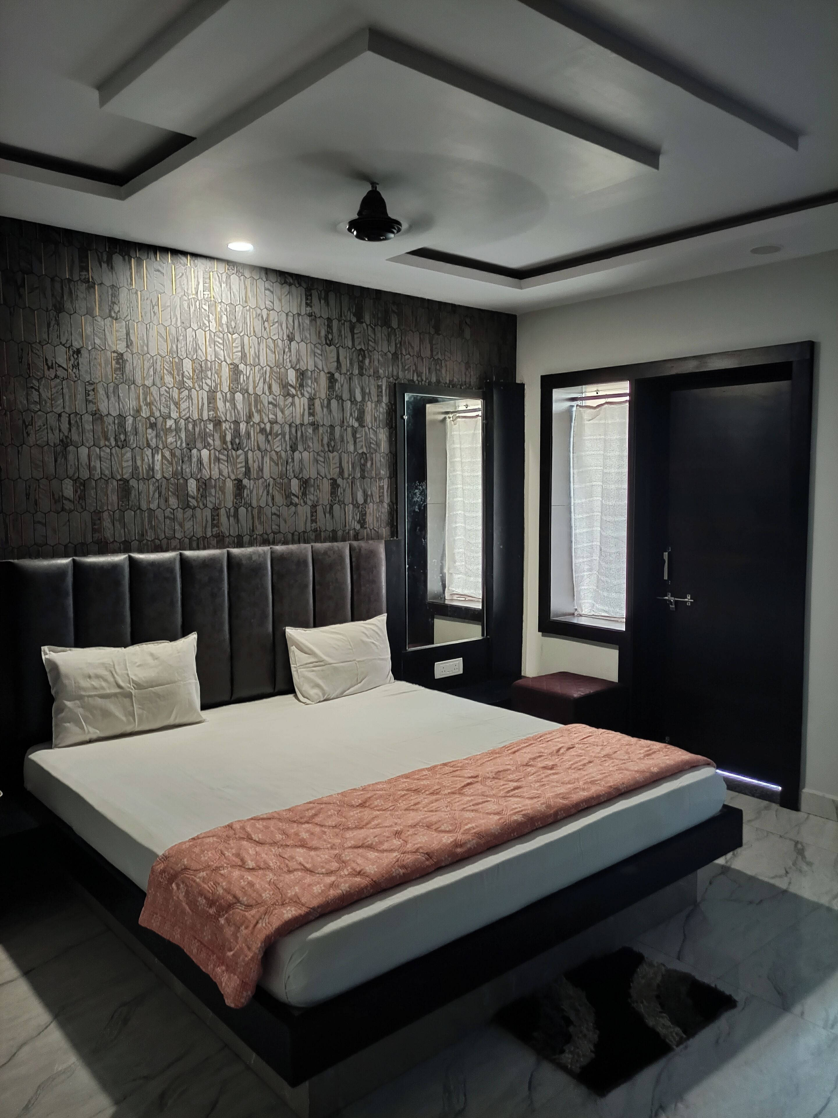 Un dormitorio moderno con una cama grande, un cabecero oscuro, un papel tapiz estampado, un espejo y una puerta oscura.