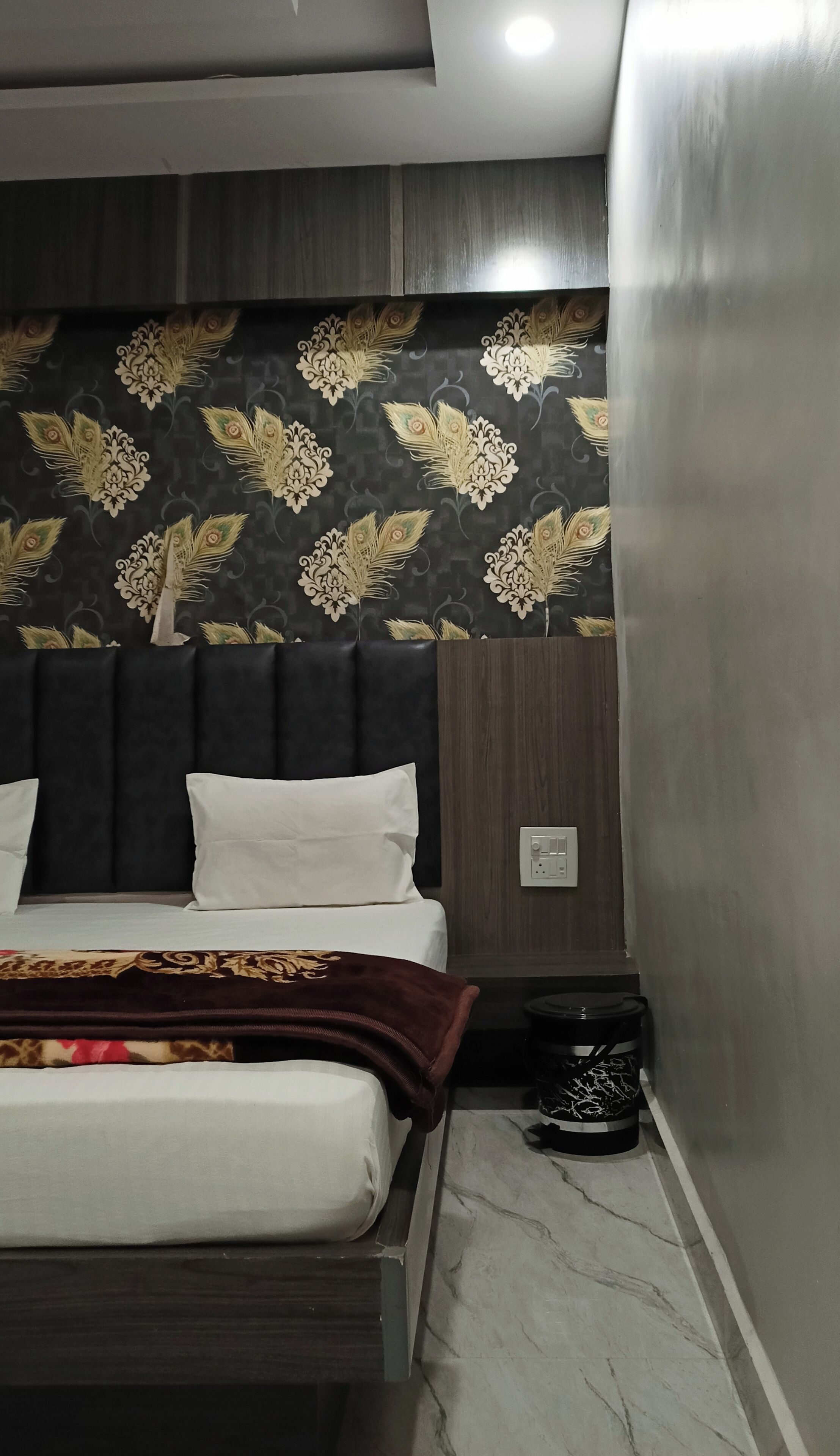 A bedroom with a bed, dark headboard, and a patterned wallpaper.