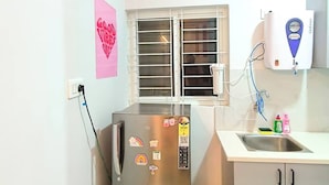 Una cocina compacta con un refrigerador de acero inoxidable, una ventana con persianas, un dispensador de agua y un lavabo.