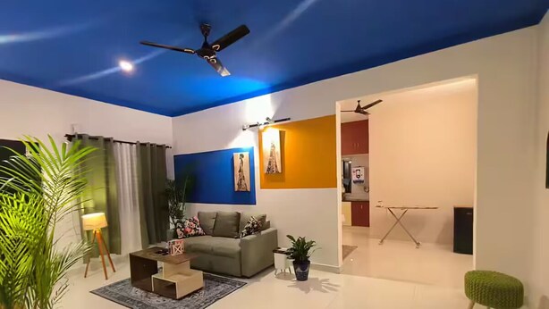 Una sala de estar moderna con un sofá gris, una mesa de centro, un taburete verde y un ventilador de techo.
