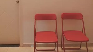 Un pasillo con dos sillas rojas, una puerta blanca y dos cuadros en la pared.