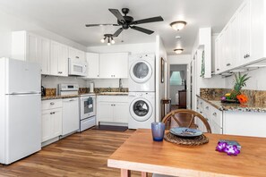 Una cocina compacta con armarios blancos, microondas, horno, lavadora y ventilador de techo.