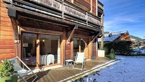 Eine Holzhütte mit Balkon, einer überdachten Außenlounge und verschneiter Landschaft.