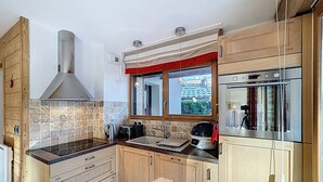Eine moderne Küche mit Holzschränken, einer Edelstahl-Dunstabzugshaube, einem Fenster mit rotem Vorhang und einem eingebauten Backofen.
