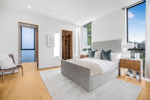 Une chambre moderne avec un grand lit, une armoire en bois, une table de chevet et une vue sur la verdure grâce à une grande fenêtre.