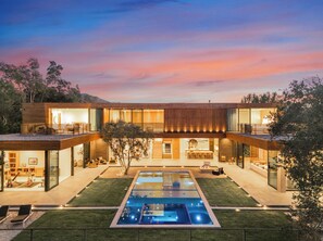 Une maison moderne à deux étages, dotée d’une grande façade vitrée, d’une piscine et d’une pelouse bien entretenue.