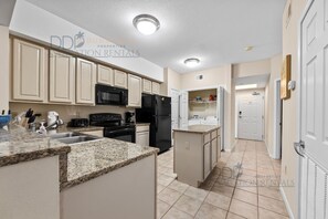 A kitchen with beige cabinets, a granite countertop, a black refrigerator, and a microwave. - Legacy Tower II 307 | Deluxe Unit with Stunning Coastal Views! (Gulfport)