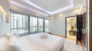 Ein modernes Hotelzimmer mit einem großen Bett, einem Balkon mit Stadtblick und einer separaten Wohnbereits mit einer Couch und einer Pflanze.