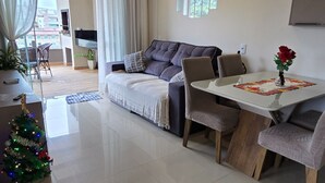 Ein modernes Wohnzimmer mit einem grauen Sofa, einem Esstisch mit Stühlen, einer kleinen Weihnachtstanne und einem Fernseher auf einem Schrank.