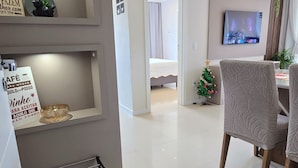 Ein modernes Wohnzimmer mit Fernseher, einem kleinen Weihnachtsbaum und einem Essbereich mit einem Stuhl.
