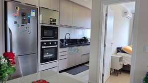 Eine moderne Küche mit Kühlschrank, Backofen, Mikrowelle und Spüle. Ein Esstisch mit dekorativer Tischdecke ist zu sehen. In der Ecke steht ein kleiner Weihnachtsbaum.