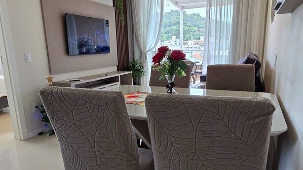 Ein modernes Wohnzimmer mit einem Flachbildfernseher, einem Esstisch mit Stühlen, einer Couch und Blick auf eine Stadtlandschaft durch große Fenster.