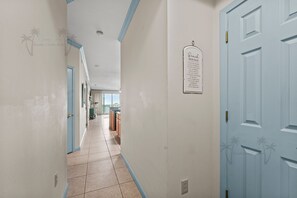 Un couloir avec une porte bleue, un panneau sur le mur et, au fond, une vue sur la cuisine.