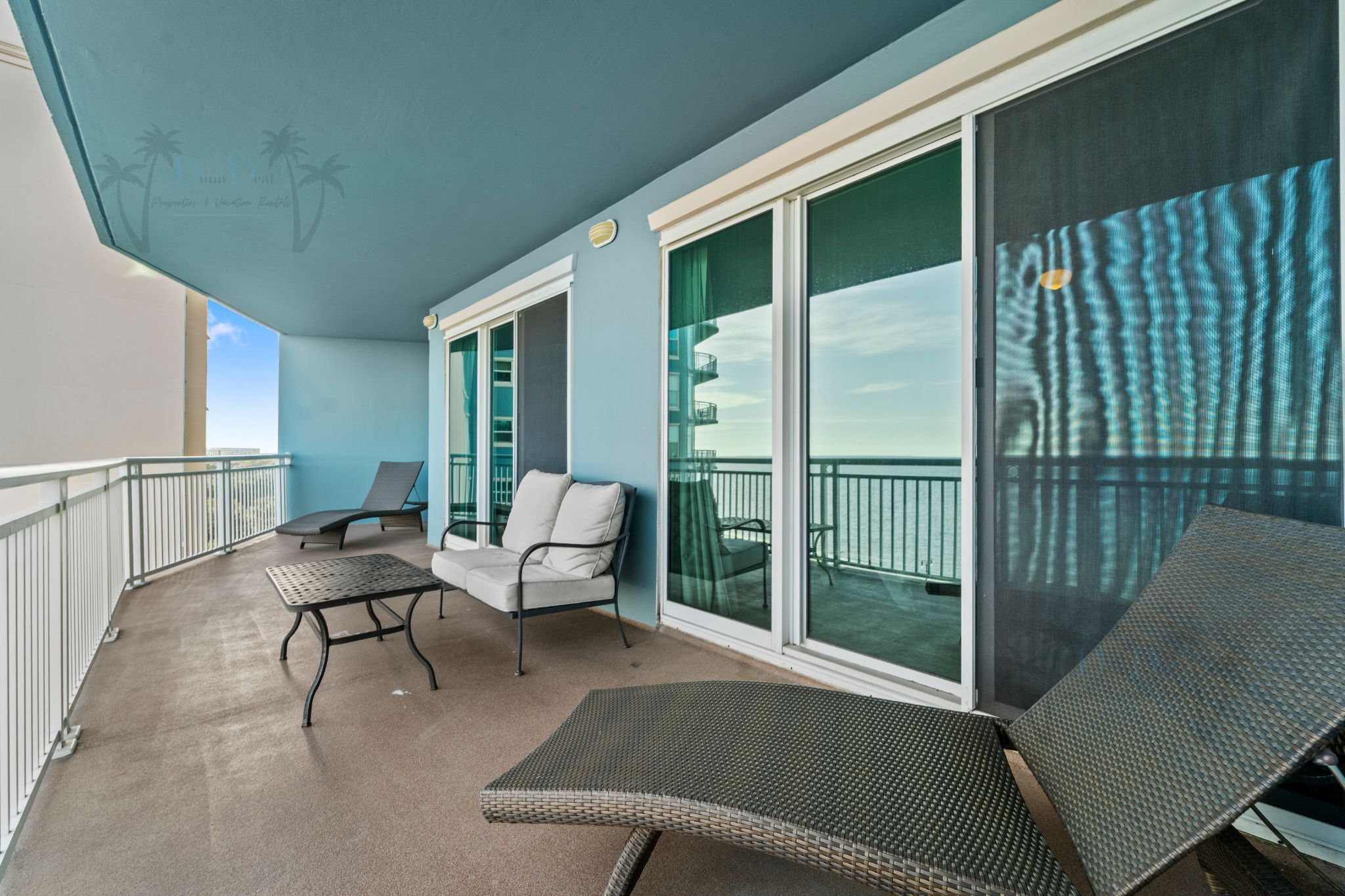 A balcony with two lounge chairs, a small table, and a glass door leading to a pool area.