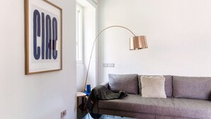 Un salon moderne avec un canapé gris, une œuvre d’art encadrée, une lampe sur pied et une fenêtre.