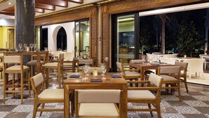 Un restaurante espacioso con varias mesas y sillas, ventanas amplias y un pilar decorativo.