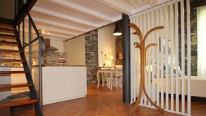 Une cuisine moderne avec un escalier en bois, un coin repas agrémenté d’un mur en pierre et une cloison blanche ornée d’un motif décoratif.
