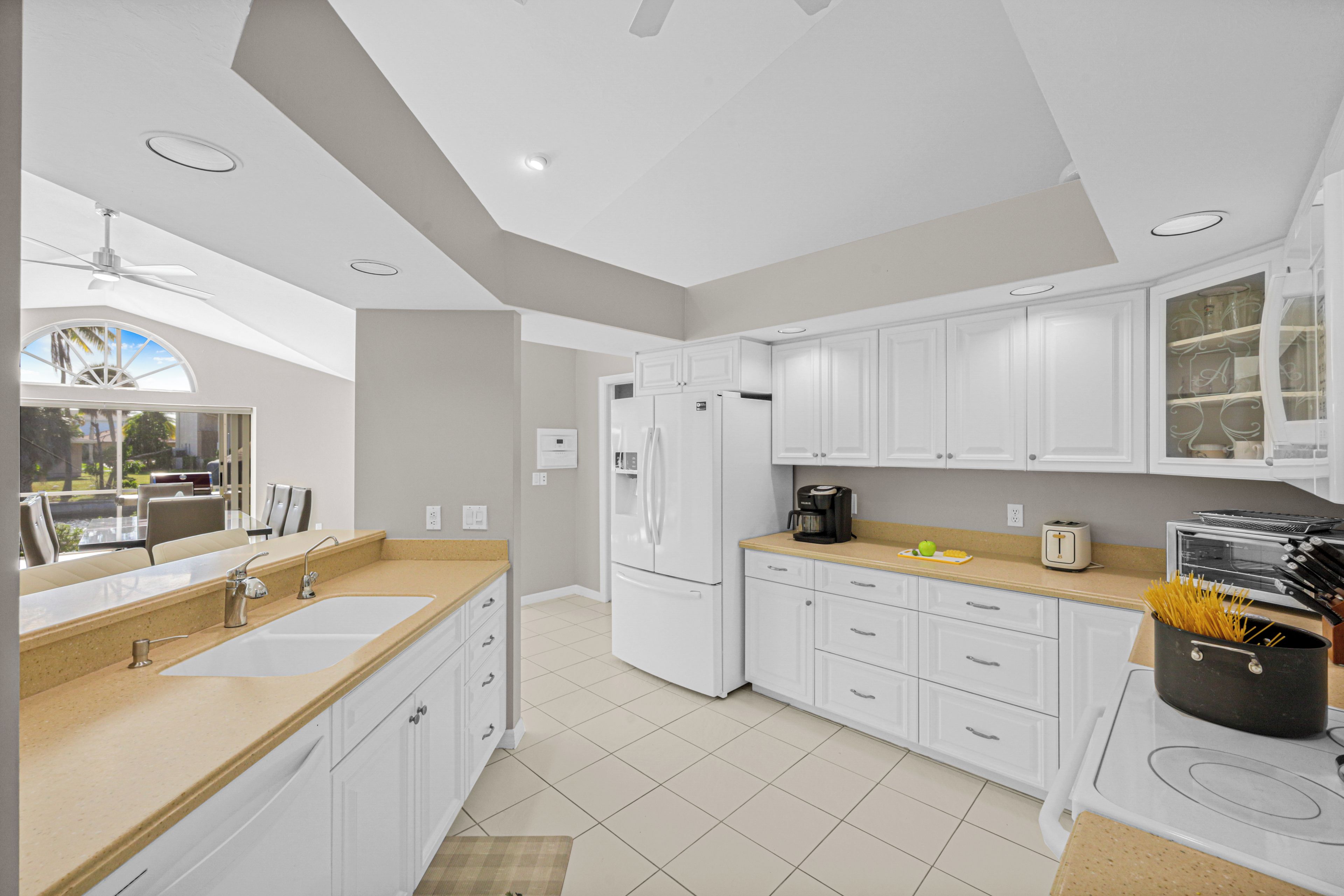 A modern kitchen with white cabinets, a double sink, and a large window overlooking a garden.