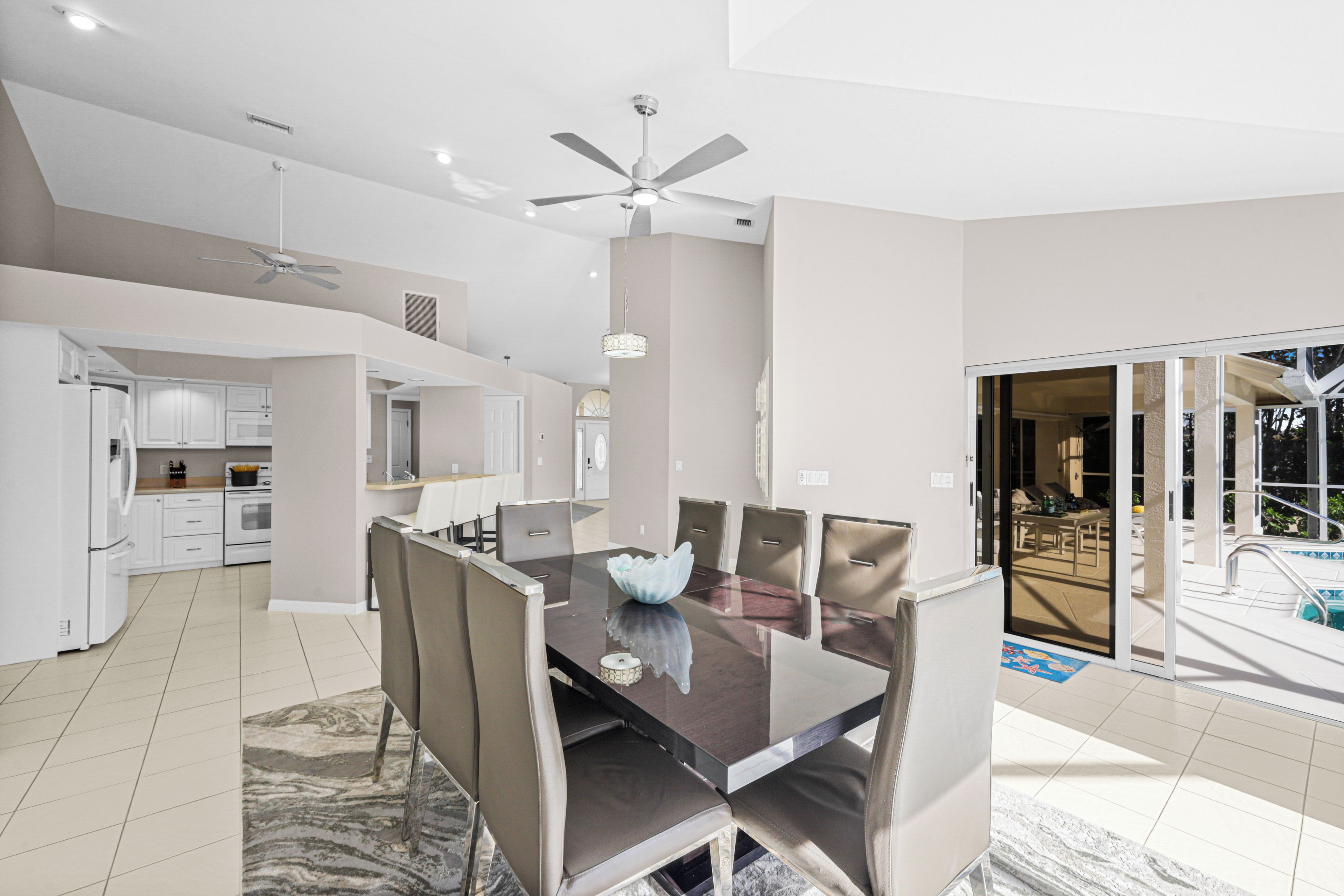 A spacious dining area with a modern glass table, comfortable chairs, and a ceiling fan.