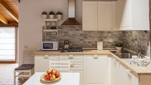 Een keuken met witte kastjes, een magnetron, een fornuis en een spoelbak. Er staan potplanten op een plank en een fruitschaal op het aanrecht.