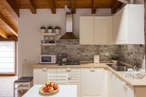 A kitchen with white cabinets, a microwave, a stove, and a sink. There are potted plants on a shelf and a bowl of fruit on the counter. - T-Rooftop - MyHomeinComo (Como)