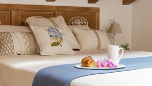 Een net opgemaakt bed met een blauwe deken, een bord met een croissant en bloemen, en een witte mok.