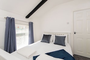 Een slaapkamer met een wit bed, grijze gordijnen en een witte deur.