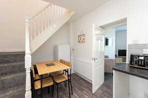 A modern kitchen with a dining area, a staircase, and a view into another room. - Toast Stays - The Merrington Fold (Kirk Merrington)