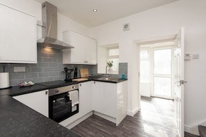 A modern kitchen with white cabinets, a black countertop, and a stainless steel range hood. - Toast Stays - The Merrington Fold (Kirk Merrington)