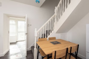 A dining area with a wooden table and chairs, a staircase with white railings, and a door leading to another room. - Toast Stays - The Merrington Fold (Kirk Merrington)