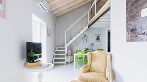 A living room with a TV, a staircase, a dining area with chairs, and a patterned armchair. - Madonnina Loft - MyHomeinComo (Moltrasio)