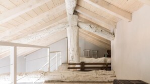 A high-ceilinged attic room with exposed wooden beams, a bed, and a staircase leading to an upper level. - Madonnina Loft - MyHomeinComo (Moltrasio)