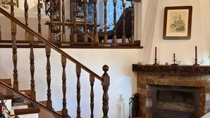 Eine Holztreppe führt zu einem Erkerbereich mit Kamin, einer Kristallleuchtre und einem gerahmten Bild an der Wand.