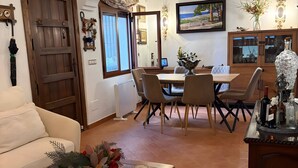 Ein Wohnzimmer mit einer Couch, einem Holztisch mit Blumen, einem Essbereich mit Tisch und Stühlen, einer Küchenzeile mit Schränken und einer Kristallleuchter.