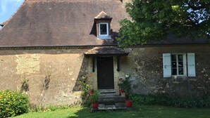 Un edificio rústico con techo inclinado y una pequeña ventana salediza, además de una puerta principal.