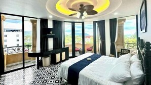 A hotel room with a bed, a ceiling fan, a TV, a balcony with a view, and a patterned floor. - Nereus Hotel (Con Dao Island)