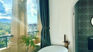 A bathroom with a bathtub, a window with a view of a building, and patterned wallpaper. - Nereus Hotel (Con Dao Island)