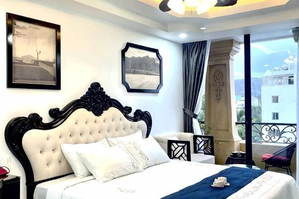 A bedroom with a large bed, a view of the city, and a balcony with a railing.