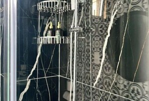 Un bagno con box doccia in vetro, una parete decorata e un pavimento piastrellato.