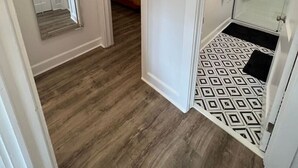 Un pasillo con piso de madera, un espejo, un termostato y una zona de ducha con azulejos estampados.