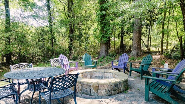 Un espacio al aire libre con una fogata de piedra, rodeado de sillas Adirondack y una mesa de metal.