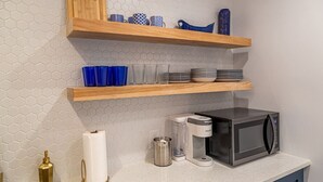 Una cocina equipada con microondas, cafetera y estantes con platos y vasos.