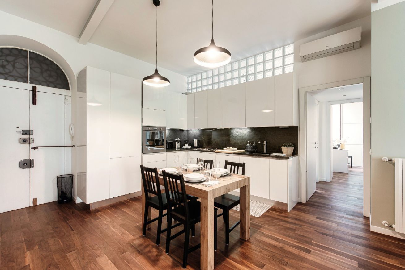 A modern kitchen with white cabinets, a wooden dining table, and pendant lighting.