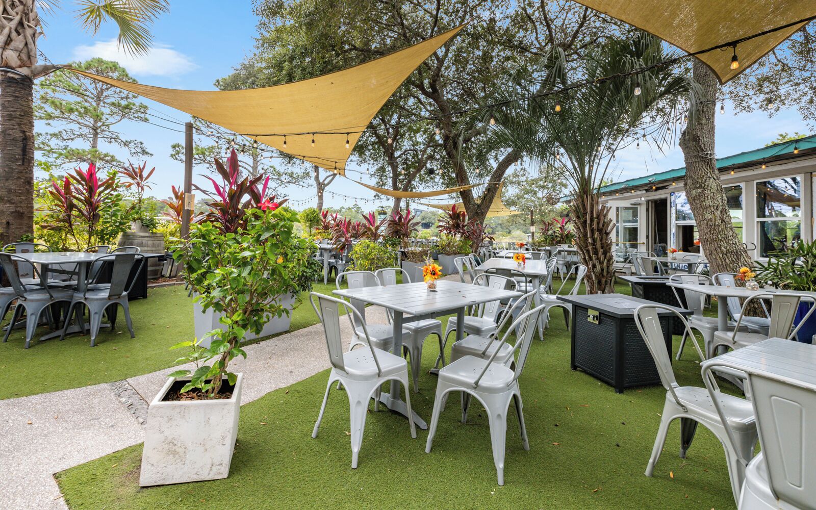 An outdoor patio with tables and chairs, surrounded by greenery and trees.