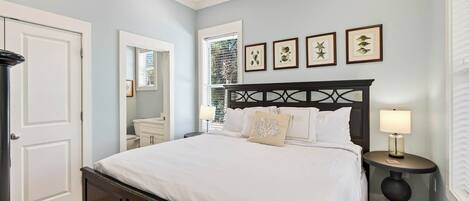 A bedroom with a bed, bedside tables, a window, and framed artwork on the wall.