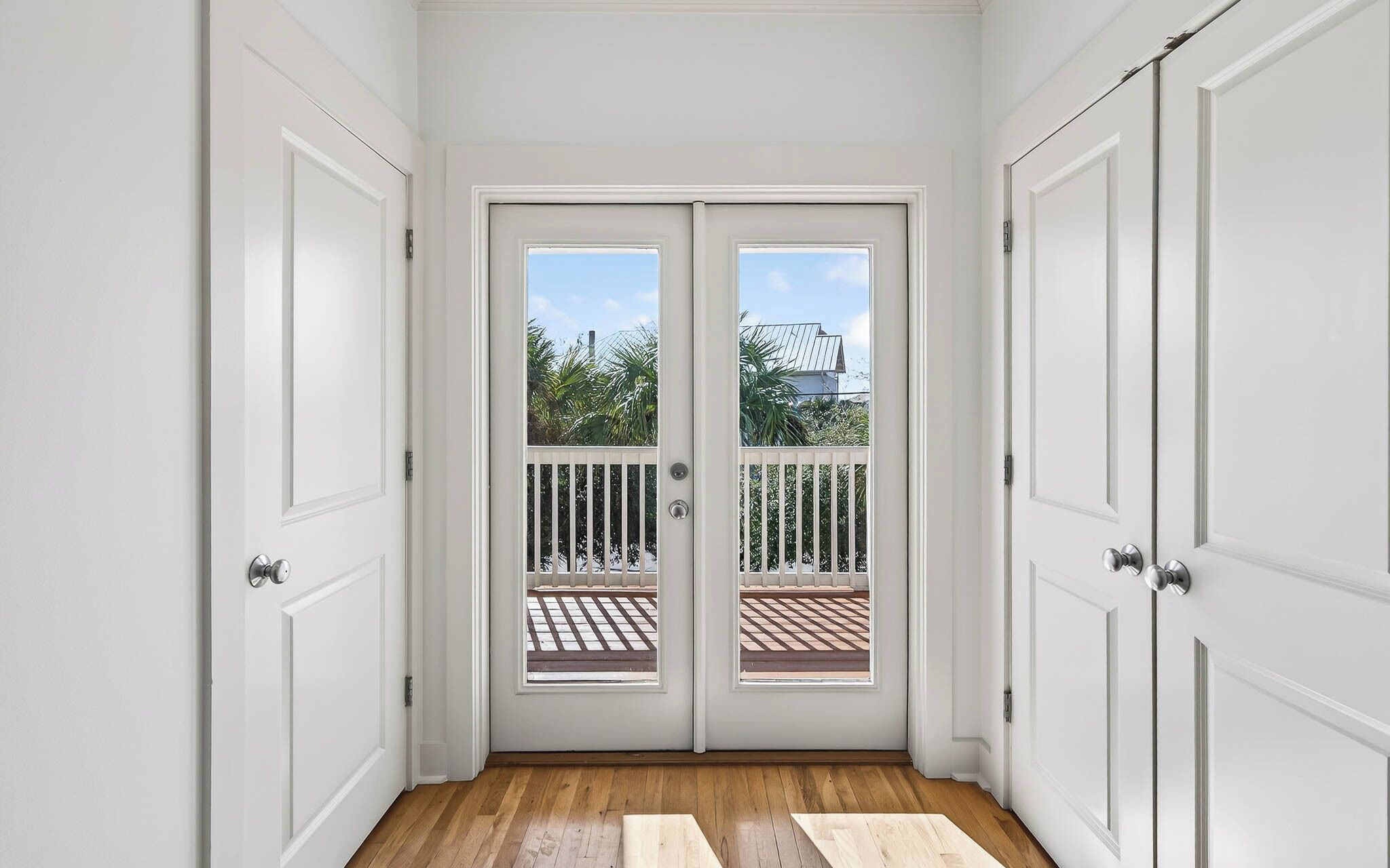 A hallway with a double door leading to an outdoor area with a wooden deck and a view of a house.