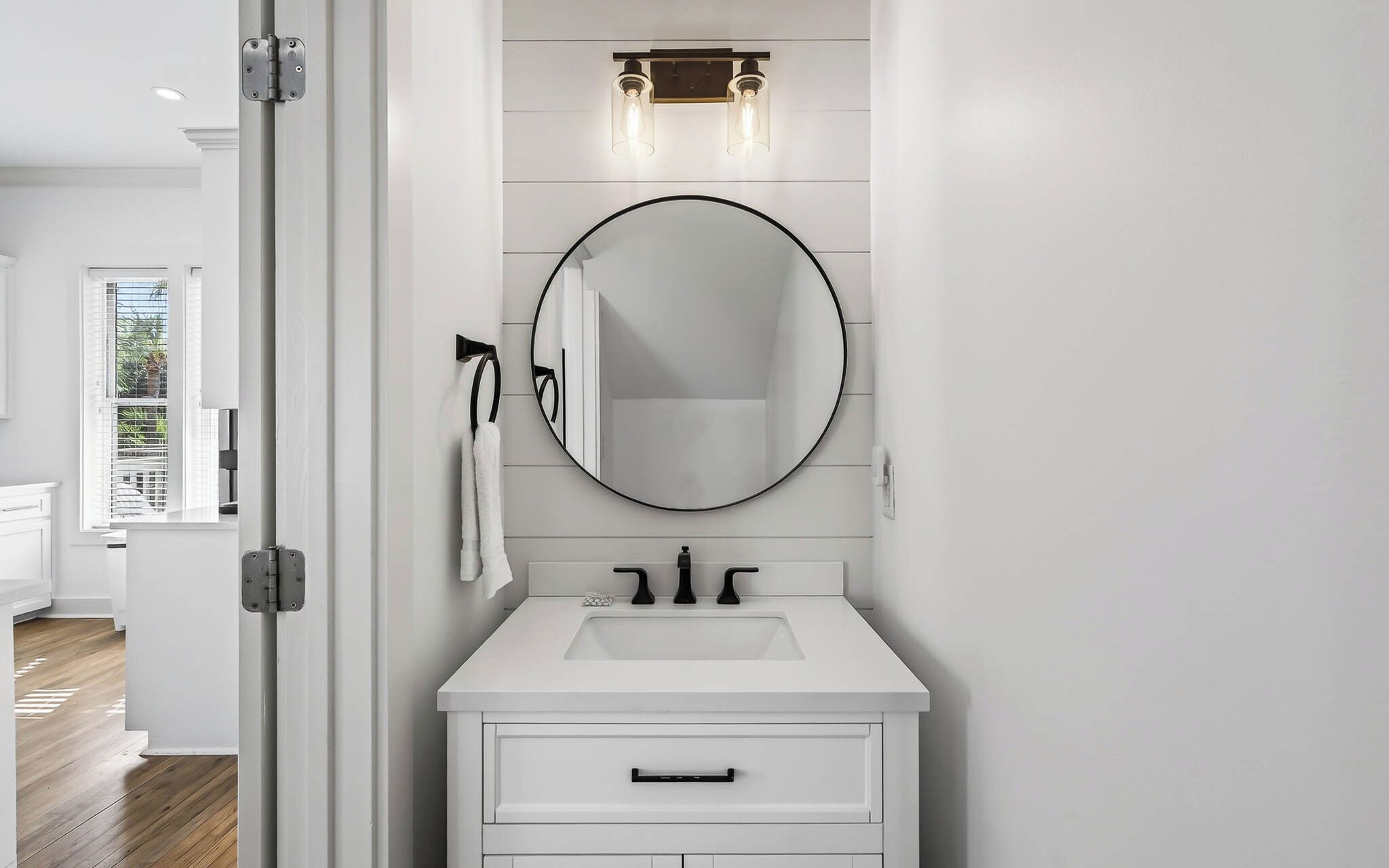 A modern bathroom with a white vanity, a round mirror, and a light fixture above the mirror.